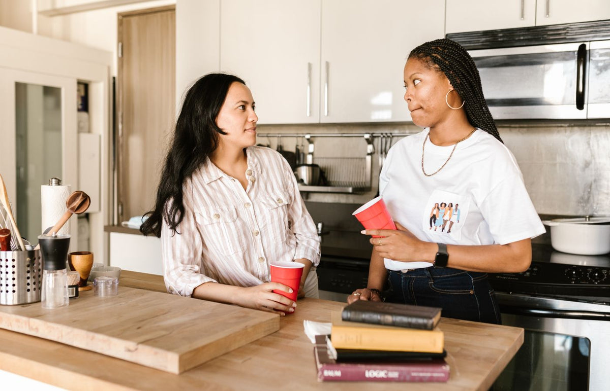Two women engaging in conversation while holding red cups in a cozy kitchen setting.