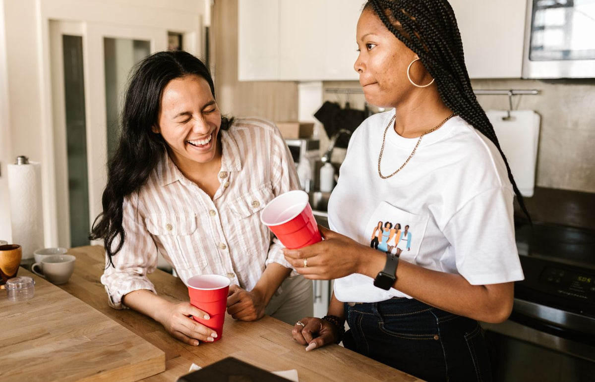 Two women having fun with red cups indoors, sharing laughter in a relaxed setting.