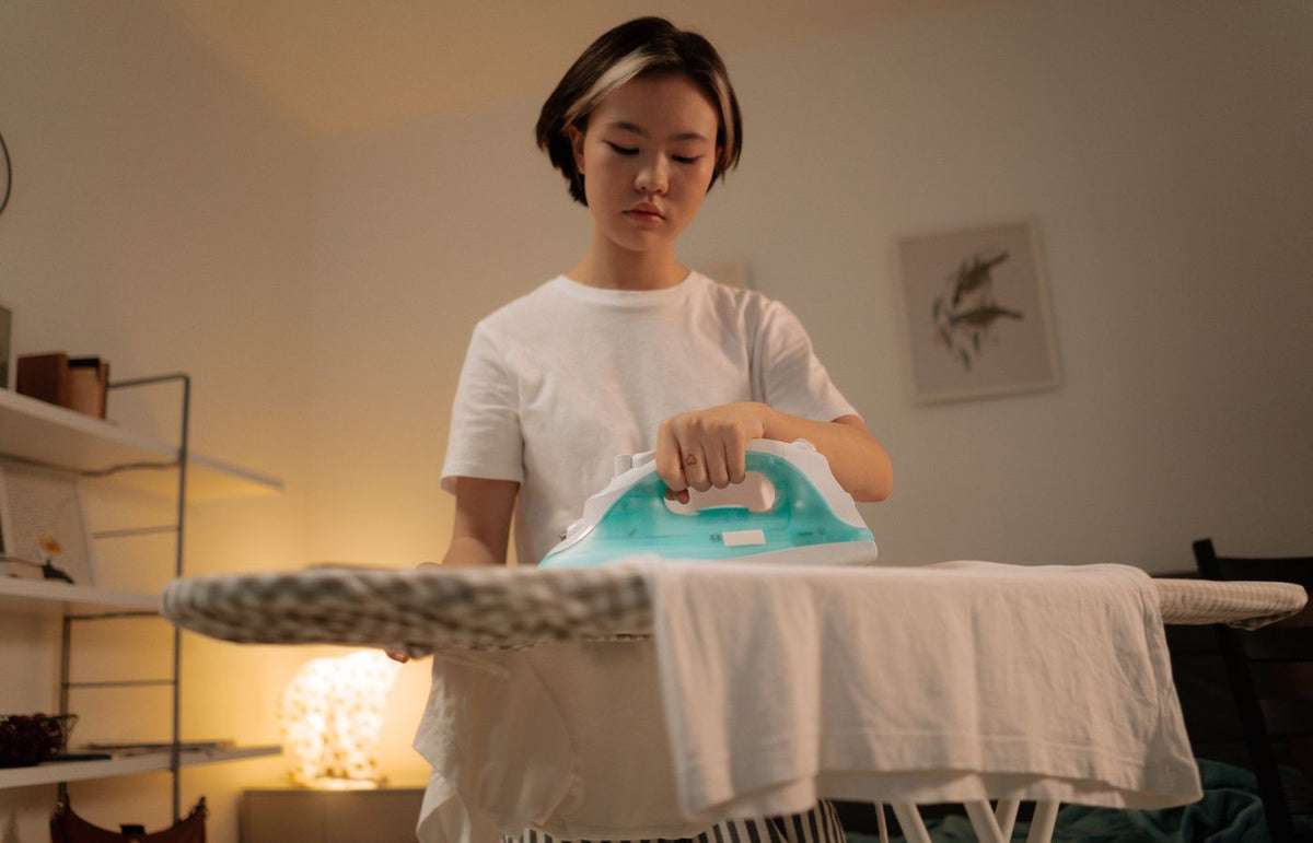 A young woman ironing a white shirt at home, focusing on casual house chores.