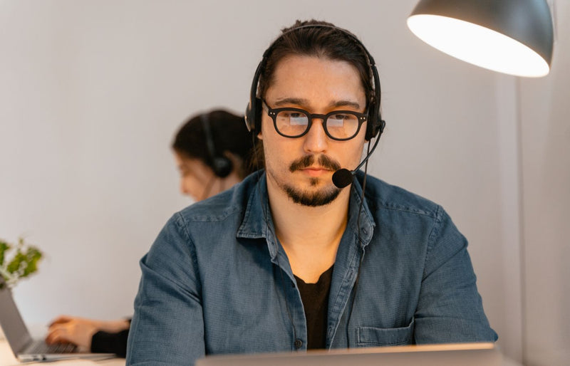 A call center agent wearing headphones, working intently at his desk in a modern office environment.