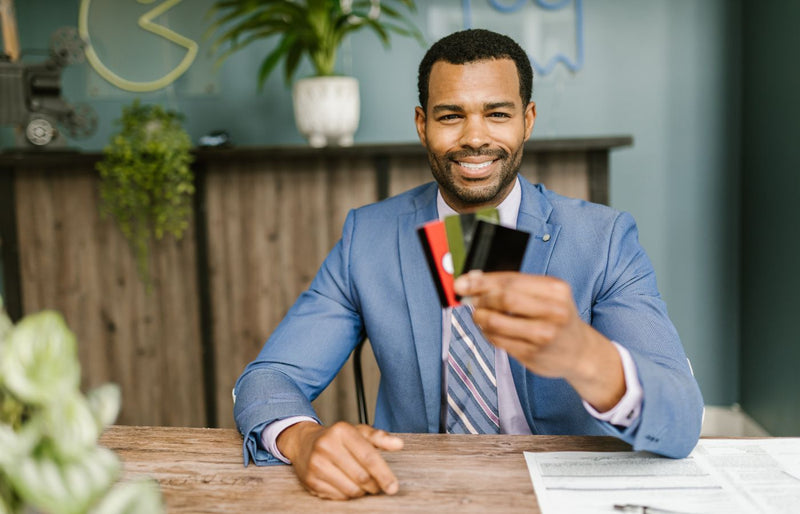 Smiling African American man in a suit holding credit cards at a business desk.