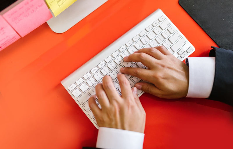Close-up of hands typing on a wireless keyboard on an orange desk, ideal for tech and business themes.