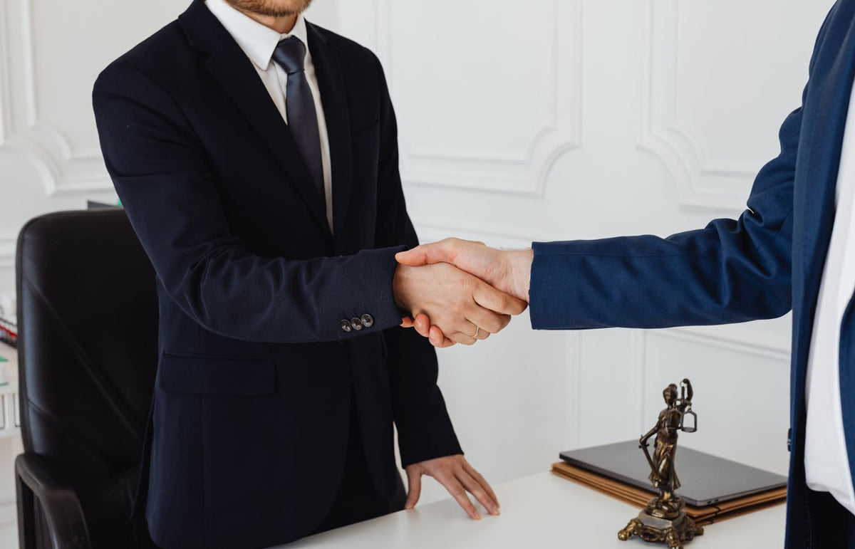 Two men in suits shaking hands in a formal office environment symbolizing an agreement.