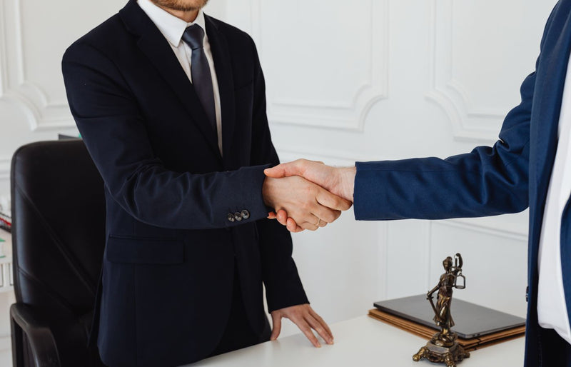 Two men in suits shaking hands in a formal office environment symbolizing an agreement.