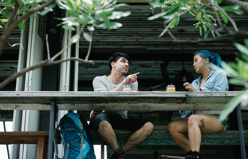 A couple enjoys drinks and conversation at an outdoor café table surrounded by greenery.