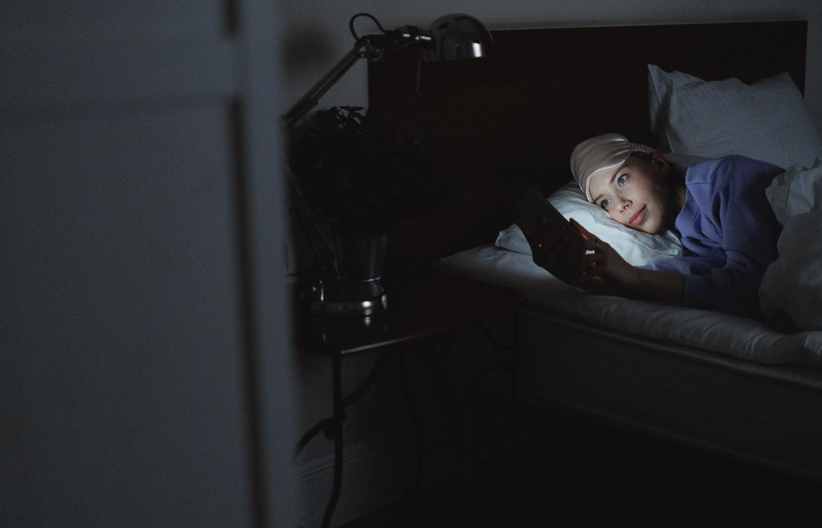 A woman in bed using a smartphone at night, her face illuminated by the screen's light.