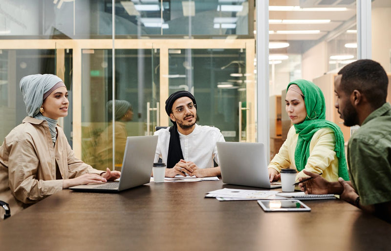 A diverse group discussing ideas in a modern office setting, using laptops and tablets.