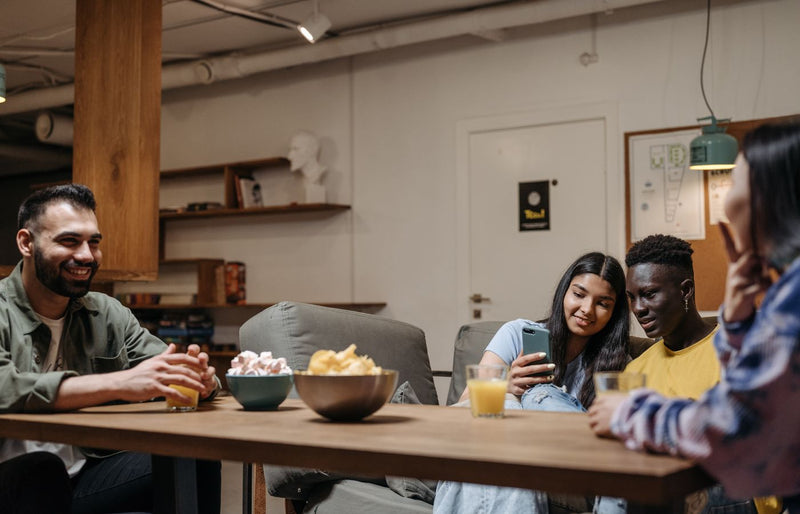 A diverse group of friends sitting together enjoying snacks and drinks indoors, capturing a moment of relaxation and bon
