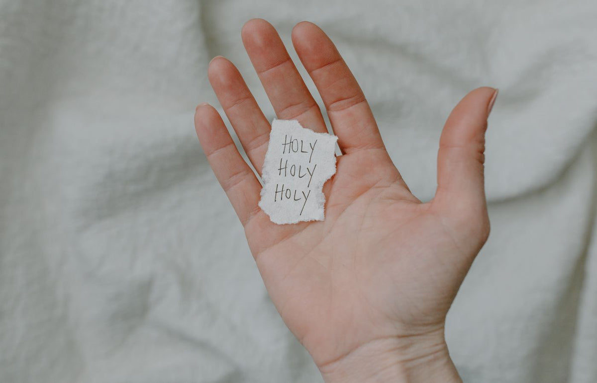 A close-up of a hand holding a paper with 'Holy' written, showing a spiritual theme.