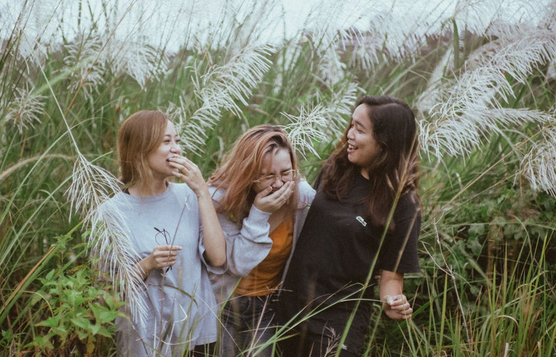 Three women enjoying a lighthearted moment amidst tall pampas grass in a natural outdoor setting.