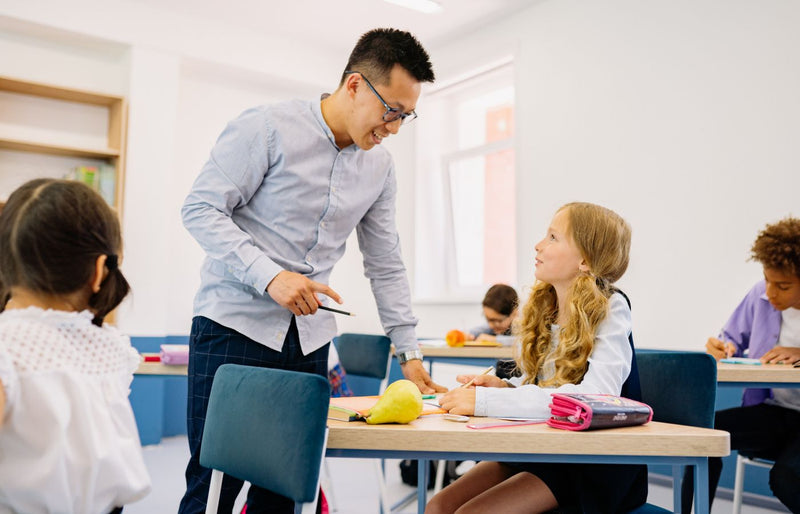 A male teacher interacting with diverse students in a bright classroom setting, promoting active learning.
