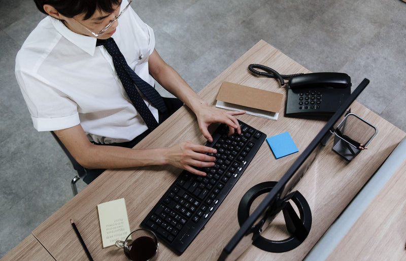 Asian man in business attire typing on a keyboard at a modern office desk.