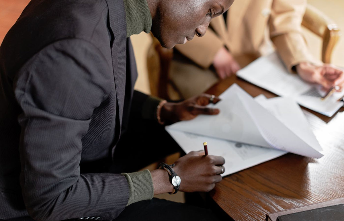 African American man focused on signing important business documents at a desk.