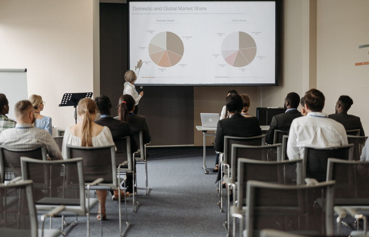 Business conference with diverse audience and speaker presenting market data.