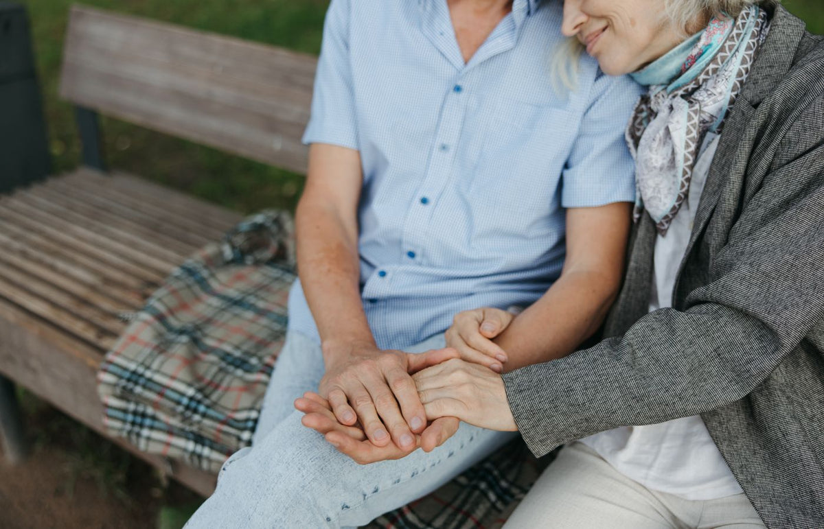 A touching moment of an elderly couple holding hands on a park bench symbolizing love and companionship.