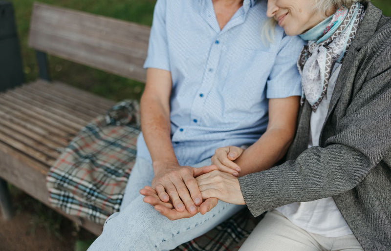 A touching moment of an elderly couple holding hands on a park bench symbolizing love and companionship.