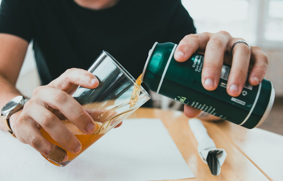 Person gently pouring beer from a can into a glass on a wooden table.