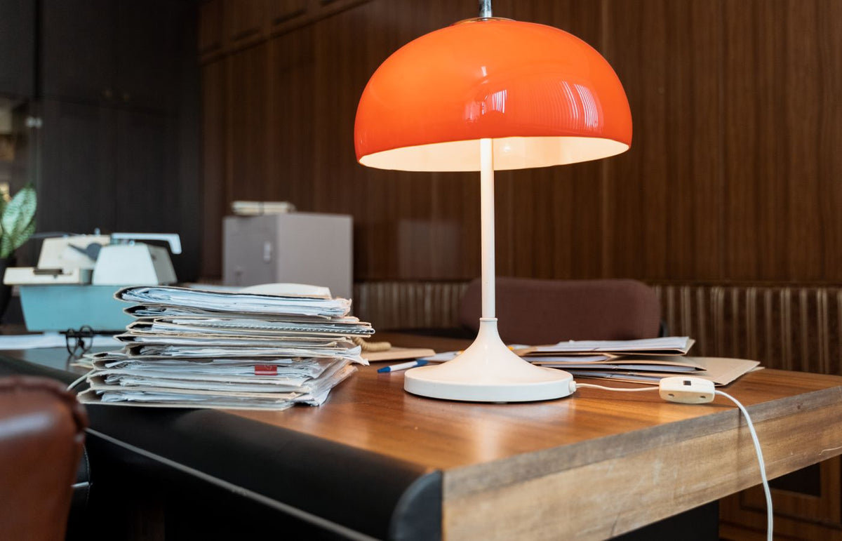 A classic office setup featuring a retro orange lamp, documents, and a wooden desk.