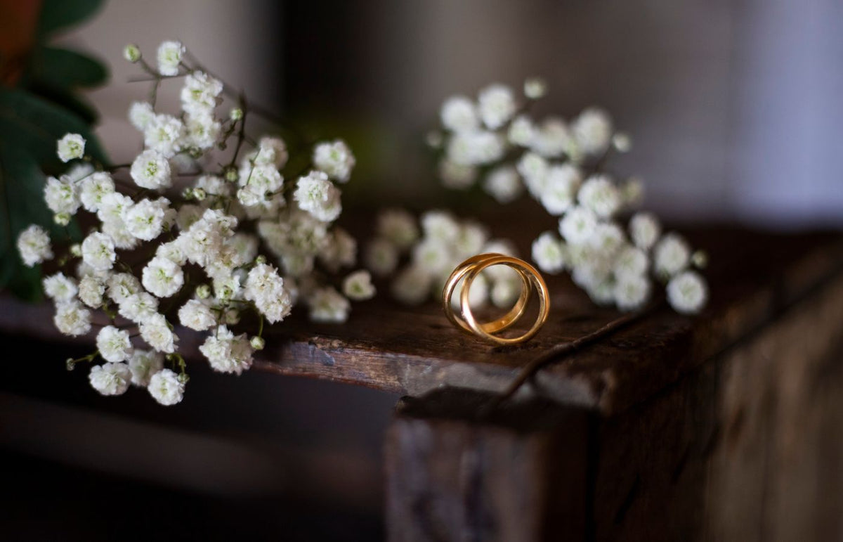 Beautiful gold wedding rings surrounded by white flowers on a rustic wooden surface. Perfect for wedding or romantic the
