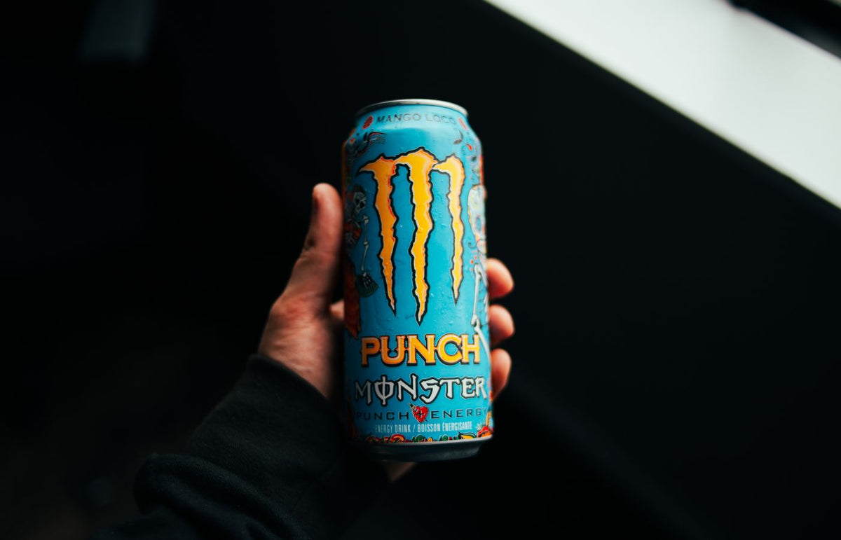 A close-up shot of a hand holding a Monster Punch energy drink can with a dark background.