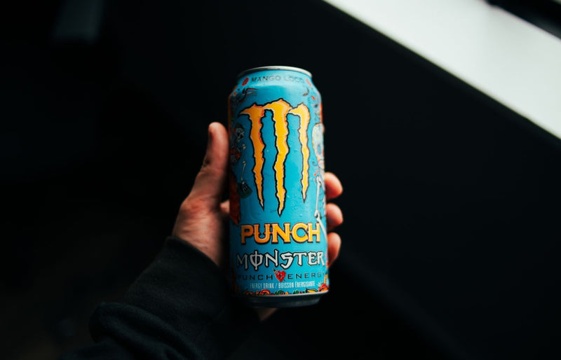 A close-up shot of a hand holding a Monster Punch energy drink can with a dark background.