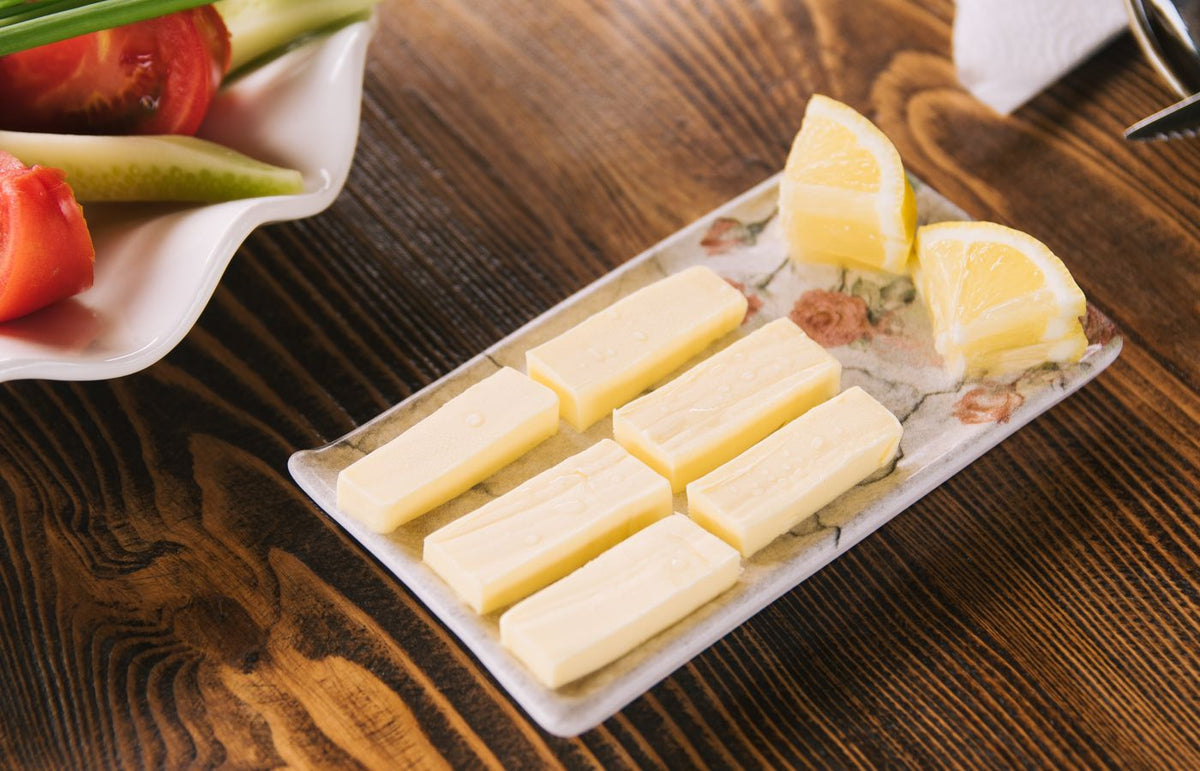 Butter sticks and lemon slices on a floral tray on a wooden table. Fresh ingredients for cooking.