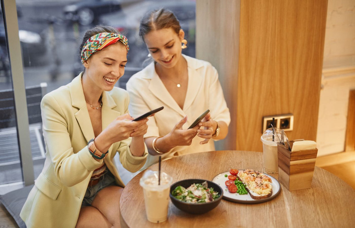 Two women enjoying drinks and snacks in a café, sharing moments and smiles.
