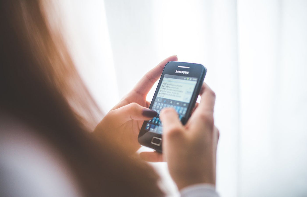 Close-up of a young woman typing on a Samsung smartphone at home. Bright indoor lighting.